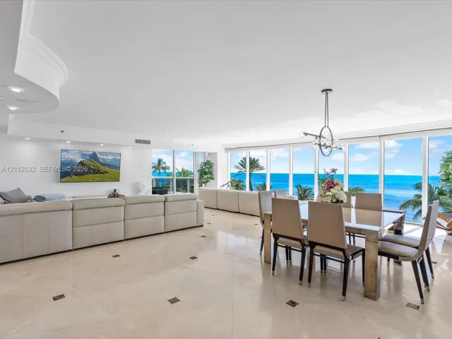Open-concept floor plan featuring expansive floor-to-ceiling windows, polished stone tile flooring with decorative inlay, recessed lighting, and a modern tiered ceiling detail