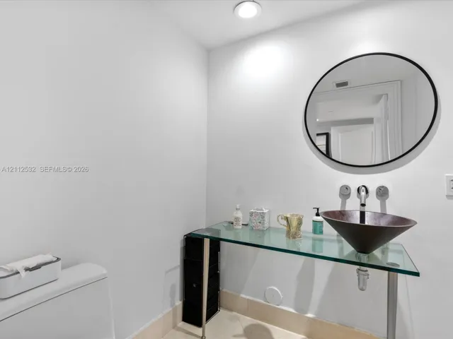 Glass-topped vanity featuring a conical vessel sink, wall-mounted faucet, and minimalist circular mirror