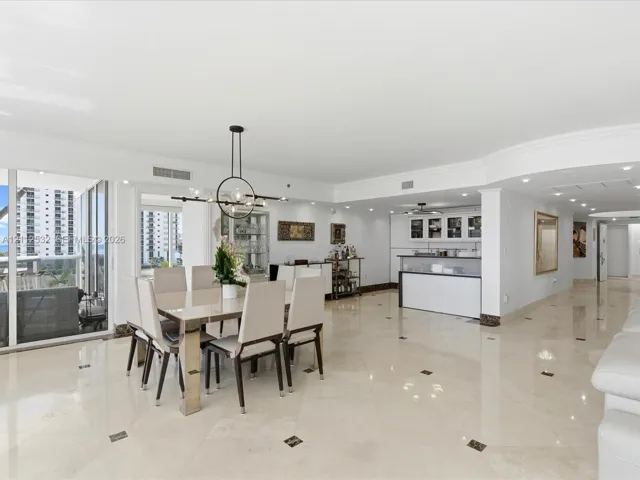 Open-concept area featuring polished stone flooring with decorative inlays, a built-in wet bar with cabinetry, recessed lighting, a modern multi-arm chandelier, and floor-to-ceiling glass sliding doors