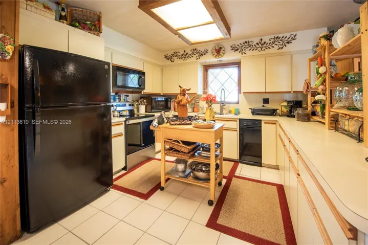 Kitchen featuring flat-panel cabinetry, a black refrigerator, a black dishwasher, a recessed ceiling light fixture with wood-trim, and ceramic tile flooring