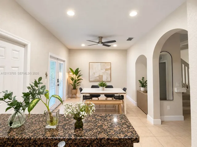 Open-concept area featuring stone-surface kitchen island, recessed lighting, double-door exterior entry, and architectural arched passageways with tile flooring