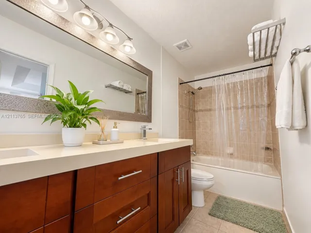 Bathroom featuring a dual-sink vanity with wood-finish cabinetry, solid surface countertop, expansive framed mirror, and tiled shower-tub combination