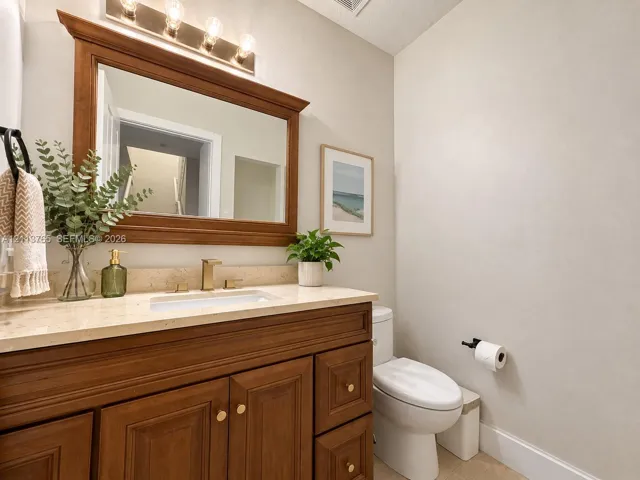 Wood-finish vanity with an integrated basin, neutral stone-finish countertop, brass-tone hardware, and a matching framed wall mirror