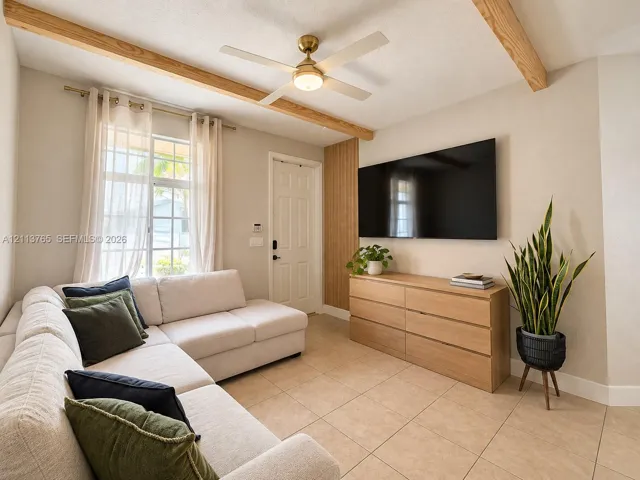Living area featuring exposed wood ceiling beams, neutral tile flooring, vertical wood slat wall accent, and a central ceiling fan with integrated lighting