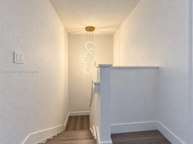 Staircase featuring wood-finish flooring, white walls, a partial-height wall railing, and a contemporary multi-ring gold-tone chandelier