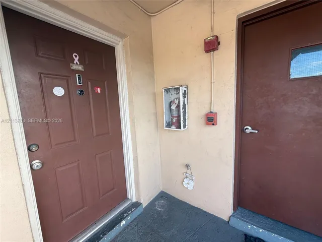 Entryway featuring two brown multi-panel doors with metallic hardware and a recessed fire extinguisher cabinet
