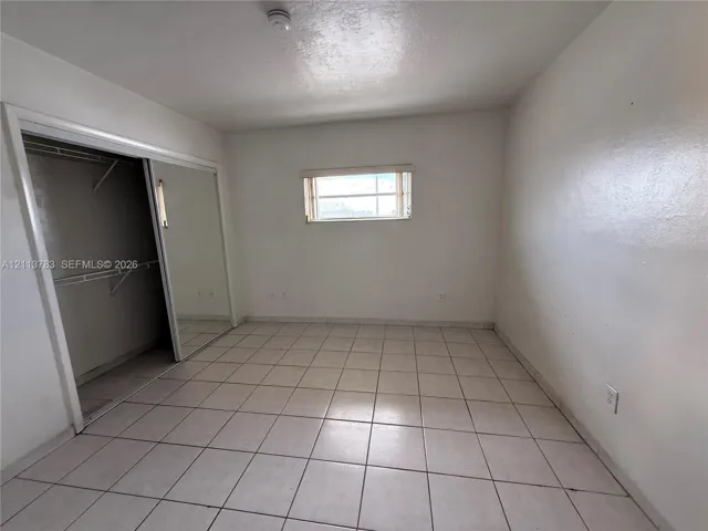Room featuring light-colored tile flooring, mirrored sliding closet doors, and a rectangular window