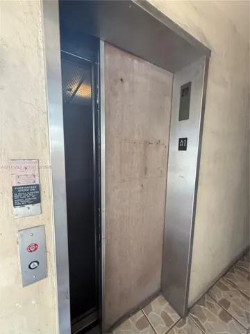Elevator featuring stainless steel framing, a protective wooden door panel, and integrated fire service controls