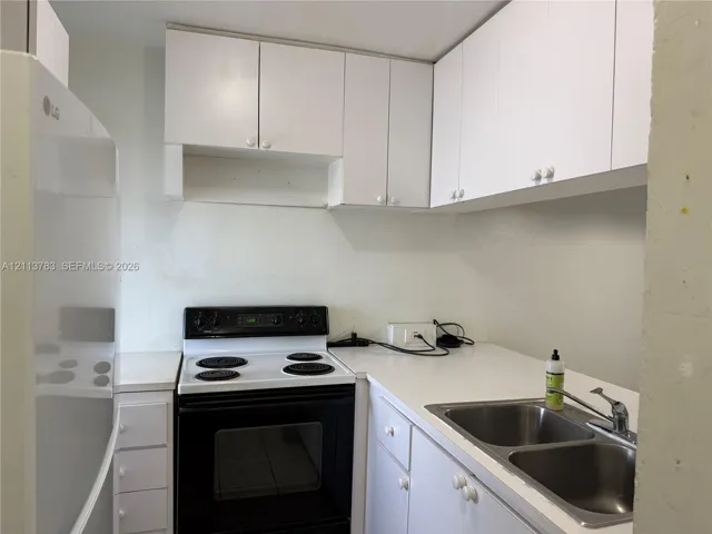 Kitchen featuring white shaker-style cabinetry, solid-surface countertops, dual-basin stainless steel sink, and a black electric range
