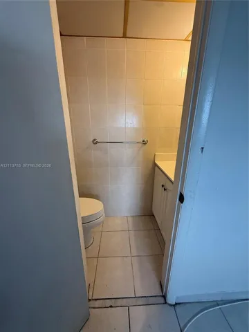 Bathroom featuring floor-to-ceiling tile work, white vanity cabinet with integrated countertop, and wall-mounted metal hardware