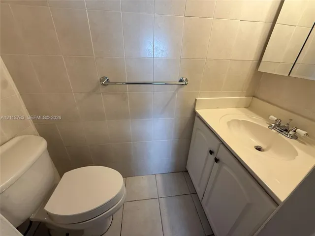 Bathroom vanity with solid-surface countertop and integrated basin, tiled wall surround, ceramic tile flooring, and polished chrome hardware