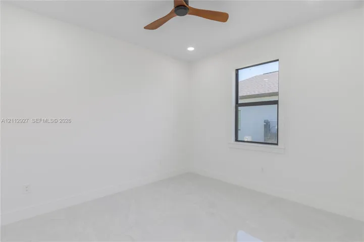 Neutral interior space featuring stone-finish tile flooring, recessed ceiling lighting, a three-blade wooden ceiling fan, and a window with black trim