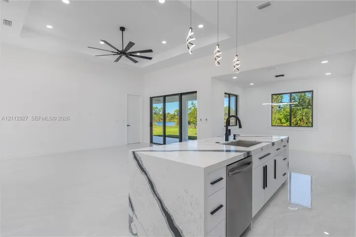 Kitchen island featuring a stone countertop with waterfall edge, matte black hardware, recessed ceiling lighting, tray ceiling with a multi-blade ceiling fan, and pendant lighting