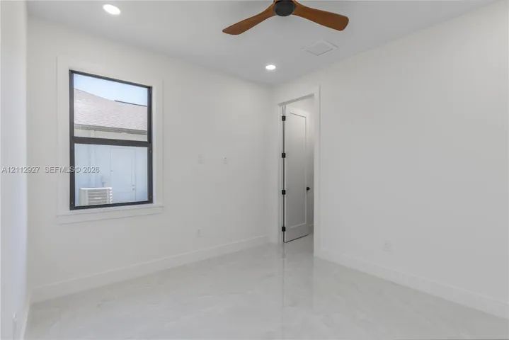 Polished stone-finish flooring, recessed lighting, wood-finish ceiling fan, and a single-panel interior door with matte black hardware