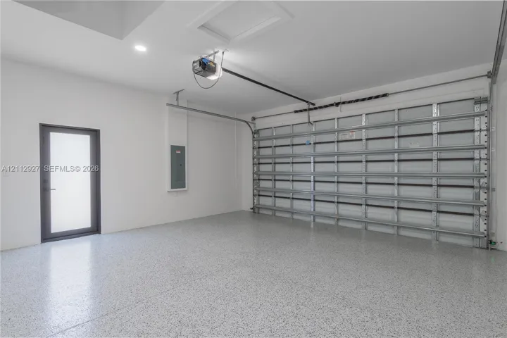 Garage space featuring an epoxy-coated floor, a large-format roll-up door, recessed lighting, and a glass-paneled entry door