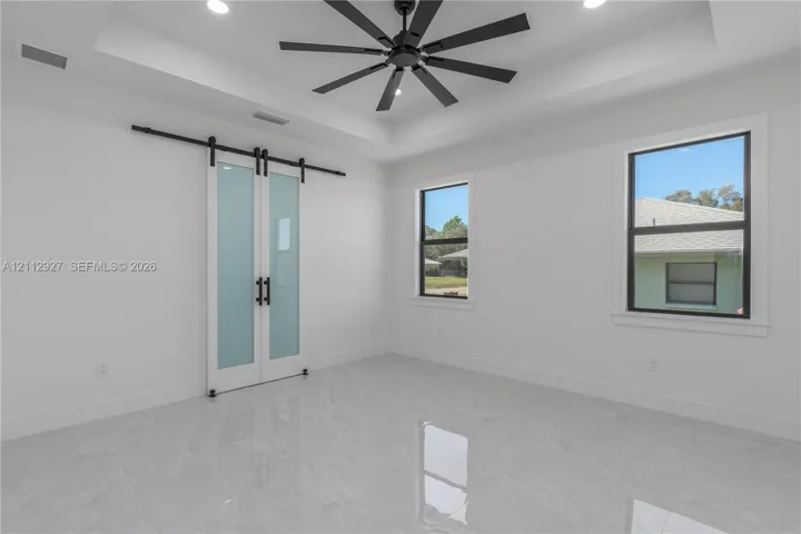 Tray ceiling, matte black ceiling fan, dual sliding barn doors with frosted glass inserts, and polished tile flooring