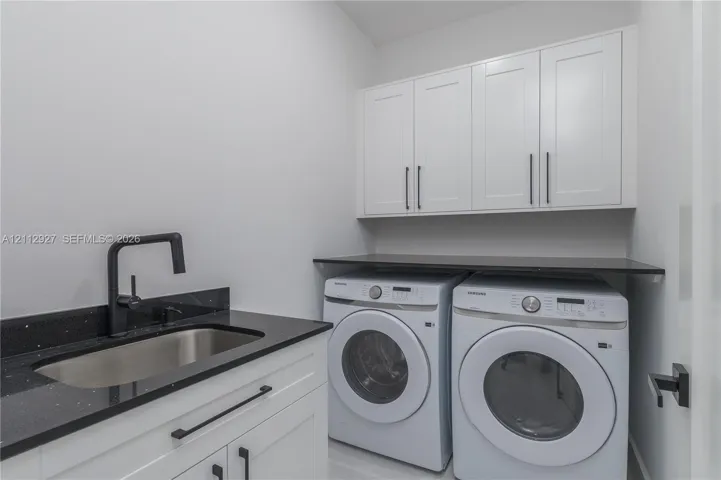 Utility room featuring white shaker-style cabinetry, dark stone-finish countertops, an undermount stainless steel sink, and a matte black gooseneck faucet