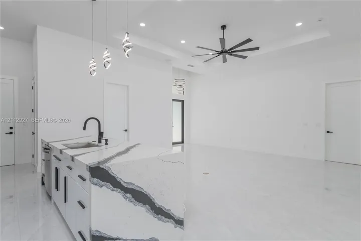 Kitchen island featuring a waterfall-edge countertop with integrated sink, matte black faucet, modern pendant lighting, tray ceiling with recessed lighting, and large-format tile flooring