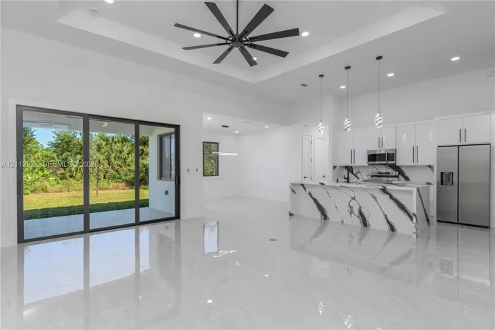 Open-concept interior featuring a tray ceiling with a multi-blade ceiling fan, large sliding glass doors, polished oversized tile flooring, and a kitchen island with stone-finish waterfall edging