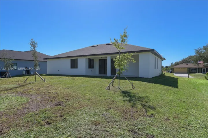 Rear elevation featuring white stucco siding, a hipped shingle roof, a covered patio area, and a spacious lawn