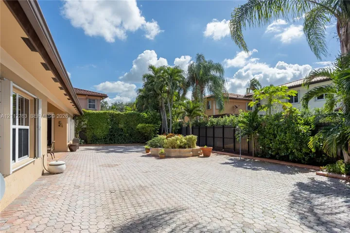 Spacious exterior courtyard featuring concrete paver flooring, a raised masonry planter, perimeter privacy fencing, and mature palm trees