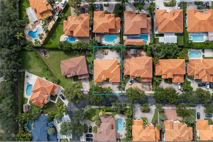 Aerial perspective of a residential property featuring a clay tile roof, a paved driveway, and mature landscaping
