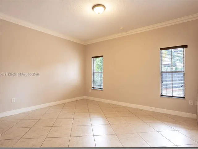 Neutral-toned room featuring diagonal tile flooring, crown molding, and two windows with horizontal blinds