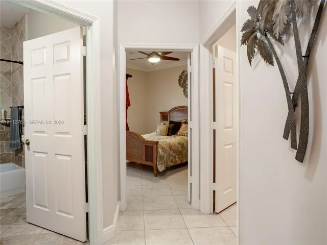 Interior hallway featuring six-panel interior doors, light-colored tile flooring, and a ceiling fan with integrated lighting