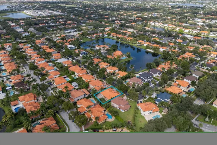 Aerial perspective of a residential property featuring a tile roof, paved driveway, and established landscaping within a suburban community