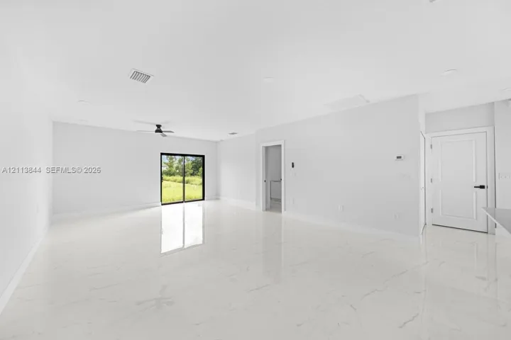 Open interior space featuring polished stone-finish tile flooring, recessed ceiling lighting, a matte black ceiling fan, and sliding glass doors