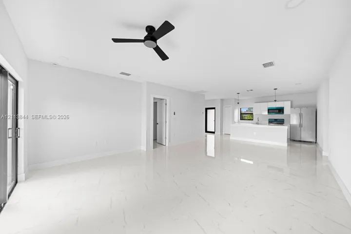 Open-concept interior featuring large-format stone-finish flooring, a matte black ceiling fan, recessed lighting, and kitchen cabinetry paired with stainless steel appliances