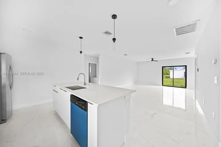Kitchen featuring a center island with a quartz countertop, undermount sink, gooseneck faucet, and built-in dishwasher, complemented by light-toned large-format tile flooring and minimalist pendant lighting
