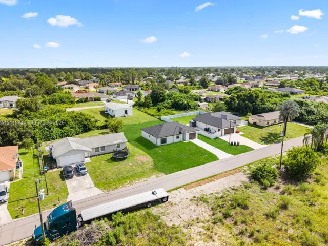 Aerial perspective of residential lots featuring paved driveways, manicured lawns, and asphalt shingle roofing