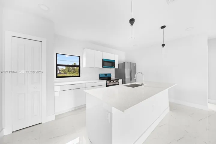 Kitchen featuring a center island with a stone-surface countertop, high-gloss white cabinetry, recessed ceiling lighting, pendant light fixtures, and white tile flooring