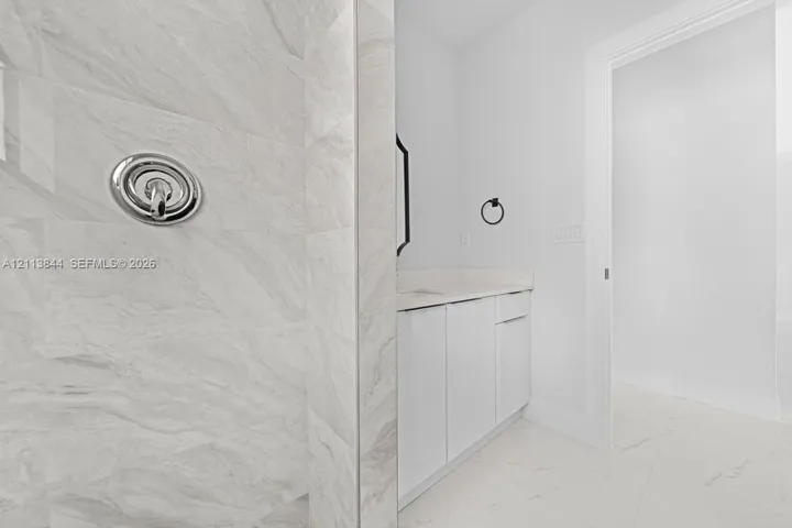 Shower featuring large-format stone-patterned wall tile and polished chrome plumbing fixtures, paired with a flat-panel vanity, light-toned countertop, and tile flooring