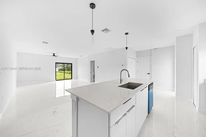 Kitchen island featuring a stone-composite countertop, undermount stainless steel sink, and sleek hardware, complemented by light-toned large-format tile flooring and minimalist pendant lighting