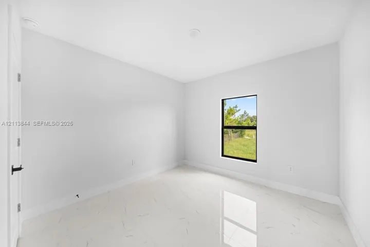Interior space featuring polished white tile flooring with grey veining, crisp neutral wall paint, and a single-pane window with a black frame