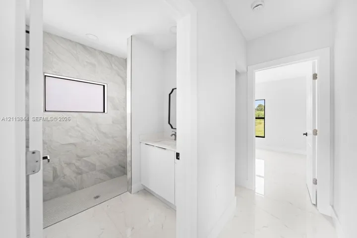Walk-in shower featuring large-format tile walls, recessed lighting, and a pebble-tiled floor, complemented by a white vanity with a stone countertop and light-colored tile flooring