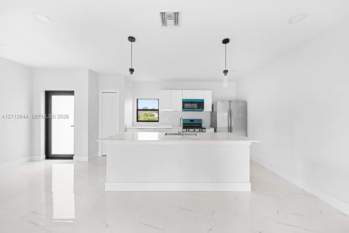 Kitchen featuring white cabinetry, a center island with a stone-finish countertop, stainless steel appliances, pendant lighting, and polished stone-finish flooring