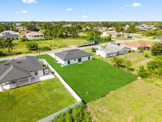 Aerial perspective of a property featuring a white stucco exterior, hip roof, expansive green lawn, and perimeter fencing