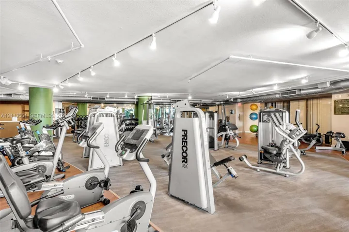Fitness center featuring track lighting, exposed structural ductwork, and structural support columns