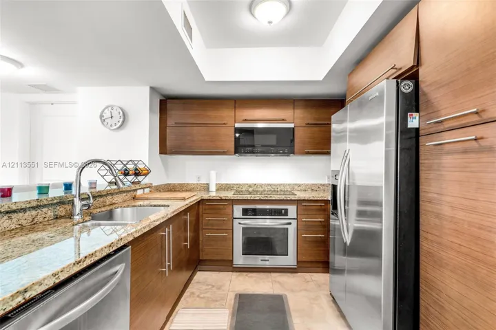 Kitchen featuring wood-finish cabinetry, stone countertops, stainless steel appliances, and a recessed ceiling element with inset lighting