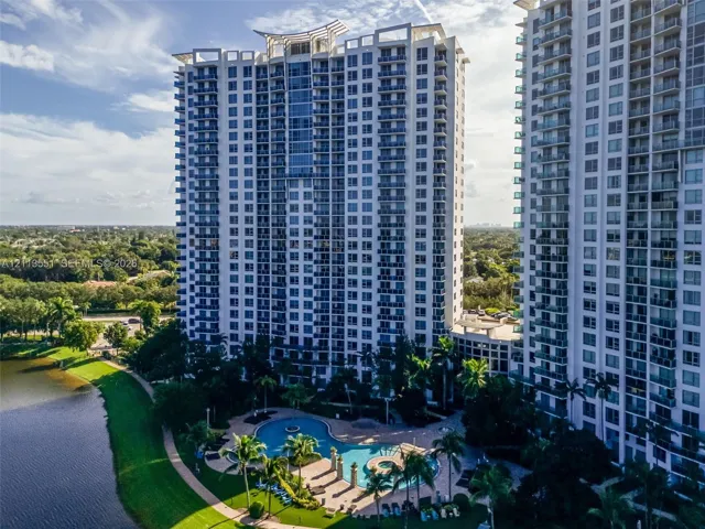 High-rise residential exterior featuring expansive glass balconies, a resort-style swimming pool, integrated spa, and manicured waterfront grounds