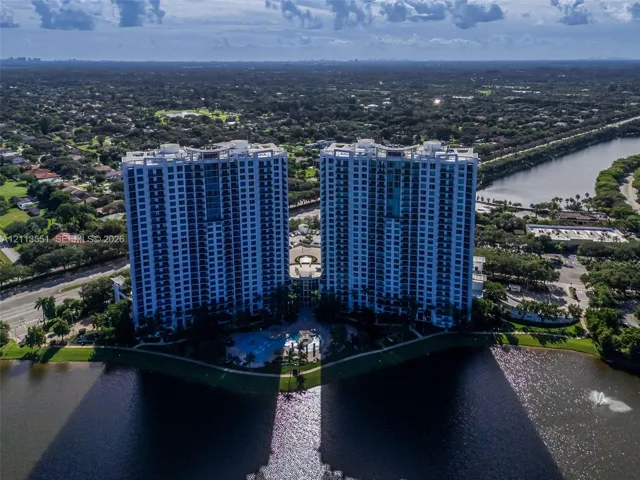 Aerial perspective of high-rise residential towers featuring balconies, ground-level pool, and water frontage