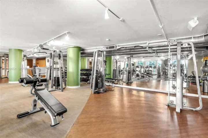 Fitness facility featuring wood-finish flooring, full-length wall mirrors, industrial-style exposed ductwork, track lighting, and structural columns