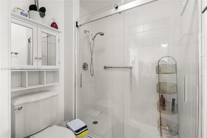 Walk-in shower with sliding glass door, white wall tiling, chrome shower fixtures, and built-in medicine cabinet with integrated shelving