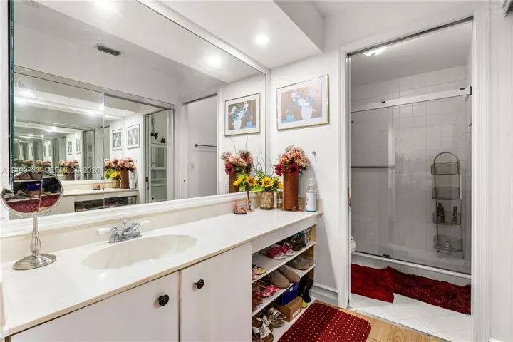 Bathroom featuring a full-width wall mirror, white vanity cabinet with a solid surface countertop, integrated sink, and an enclosed shower with sliding glass doors
