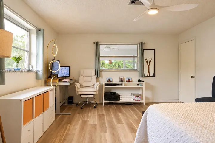 Wood-finish flooring, white walls, dual windows with natural light, and a white ceiling fan with integrated lighting