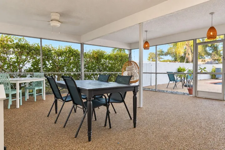 Screened-in patio featuring textured aggregate flooring, dual pendant lighting, a ceiling fan, and a glass-paneled entry door