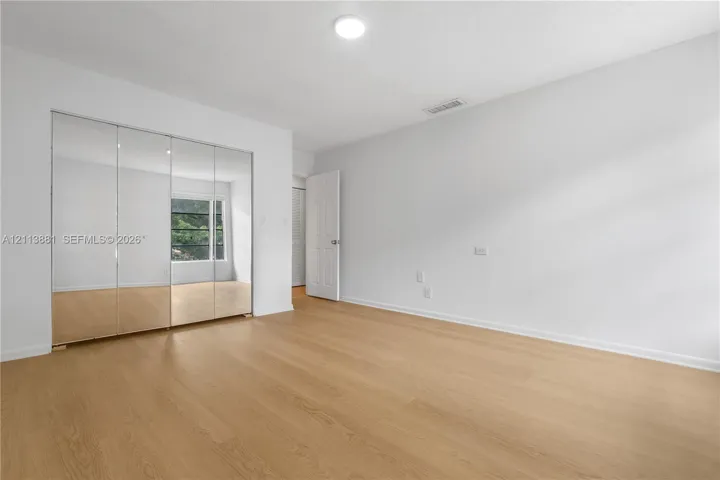 Room featuring wood-finish flooring, floor-to-ceiling mirrored sliding closet doors, a multi-panel door, and a single-light fixture